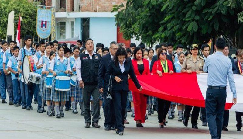 Estudiantes y banda escolar participando en un desfile cívico por las calles del distrito.